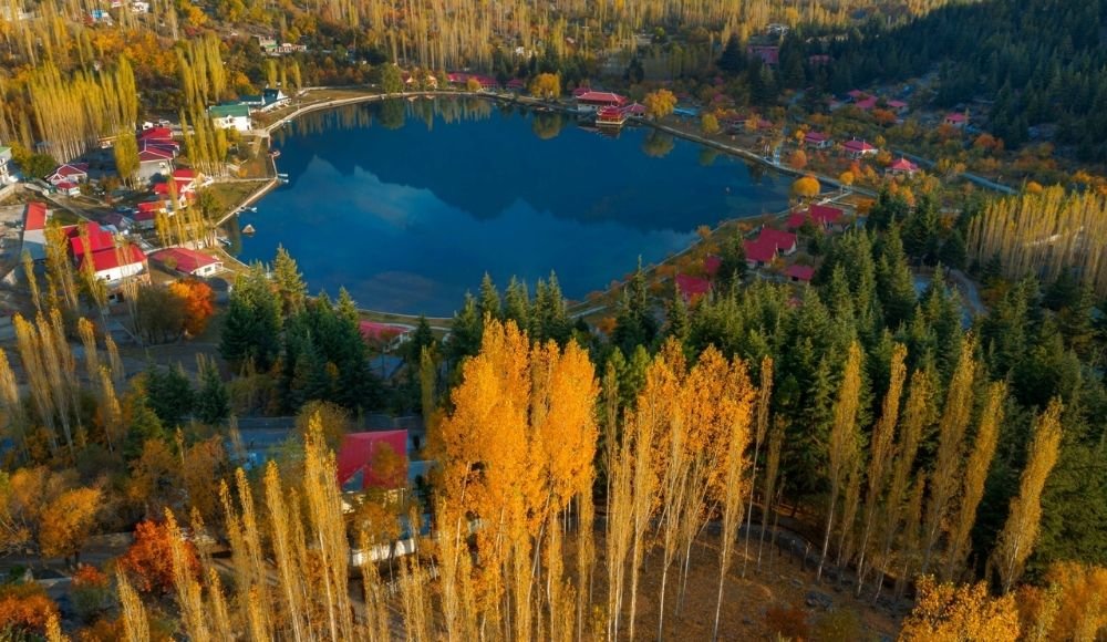 Aerial view of Shangrila Resort in Skardu during autumn, showing red-roofed cottages around a heart-shaped lake surrounded by golden and green foliage.